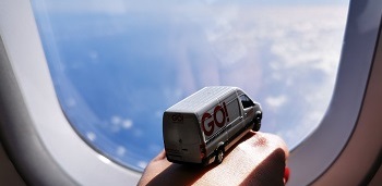 Miniatur GO! Transporter blickt aus dem Flugzeugfenster. Das Flugzeug fliegt über das Meer