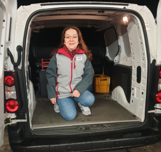 GO! Kurierin hockt, mit einem Knie auf dem Boden im hinteren Teil des GO! Transporters. Die Hintertür ist offen.