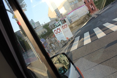Ein Blick aus dem GO! Transporter, auf die Straße. Hinter einem Zebrastreifen ist dein GO! Werbeplakat zu sehen.