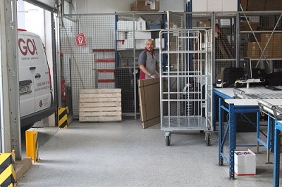 GO! Kurier holt ein großes und flaches Paket aus dem Lager, um es in den Transporter zu bringen