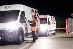 Zwei GO! Transporter parken am Straßenrand bei Nacht. Ihre Standlichter sind eingeschaltet. Ein Mann in orangener Warnschutzweste gibt dem Fahrer ein Dokument